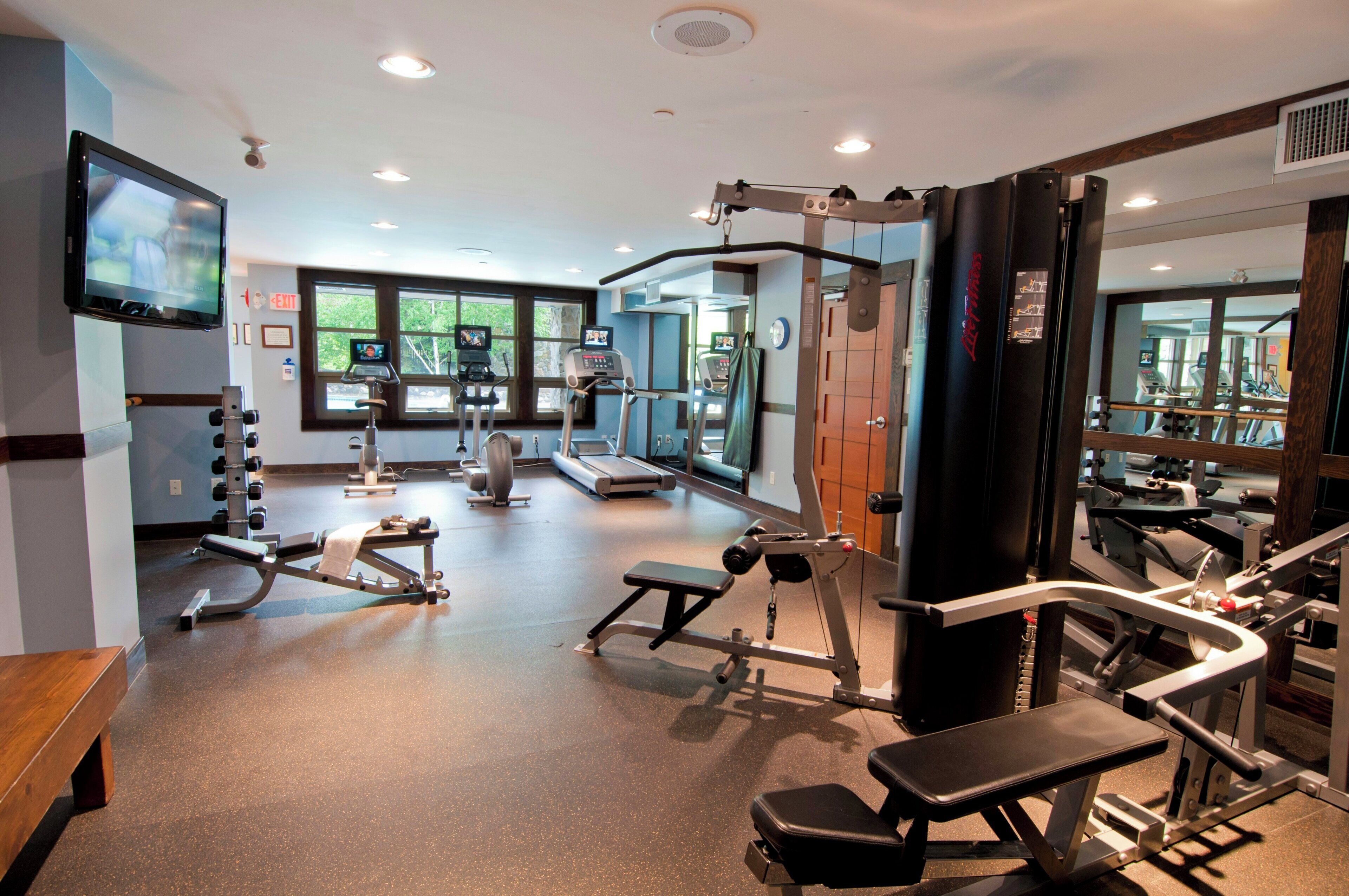 Academia com equipamentos de ginástica, um banco e uma tela de televisão.