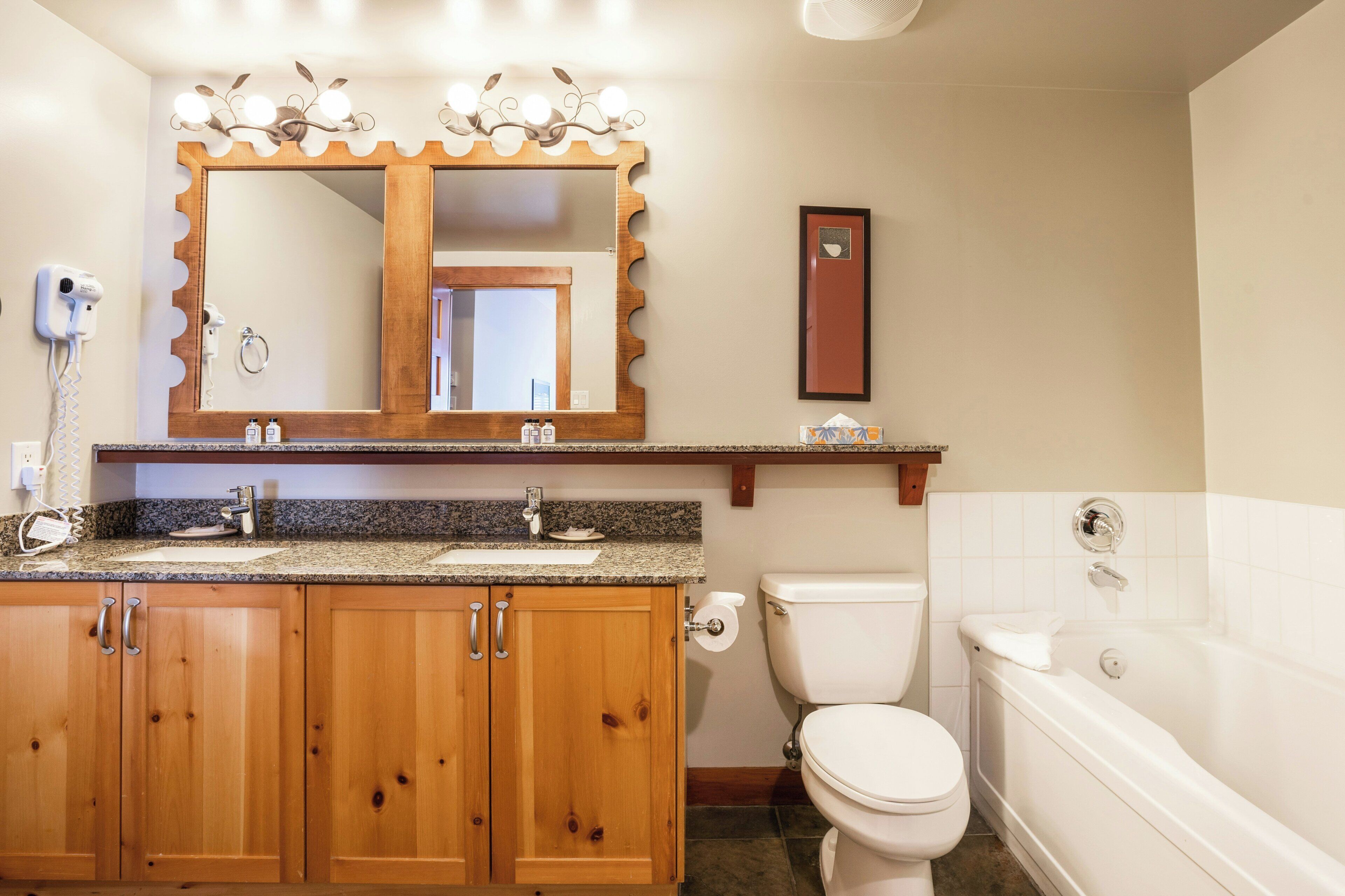 A bathroom with a wooden vanity, a large mirror, a toilet, and a bathtub.