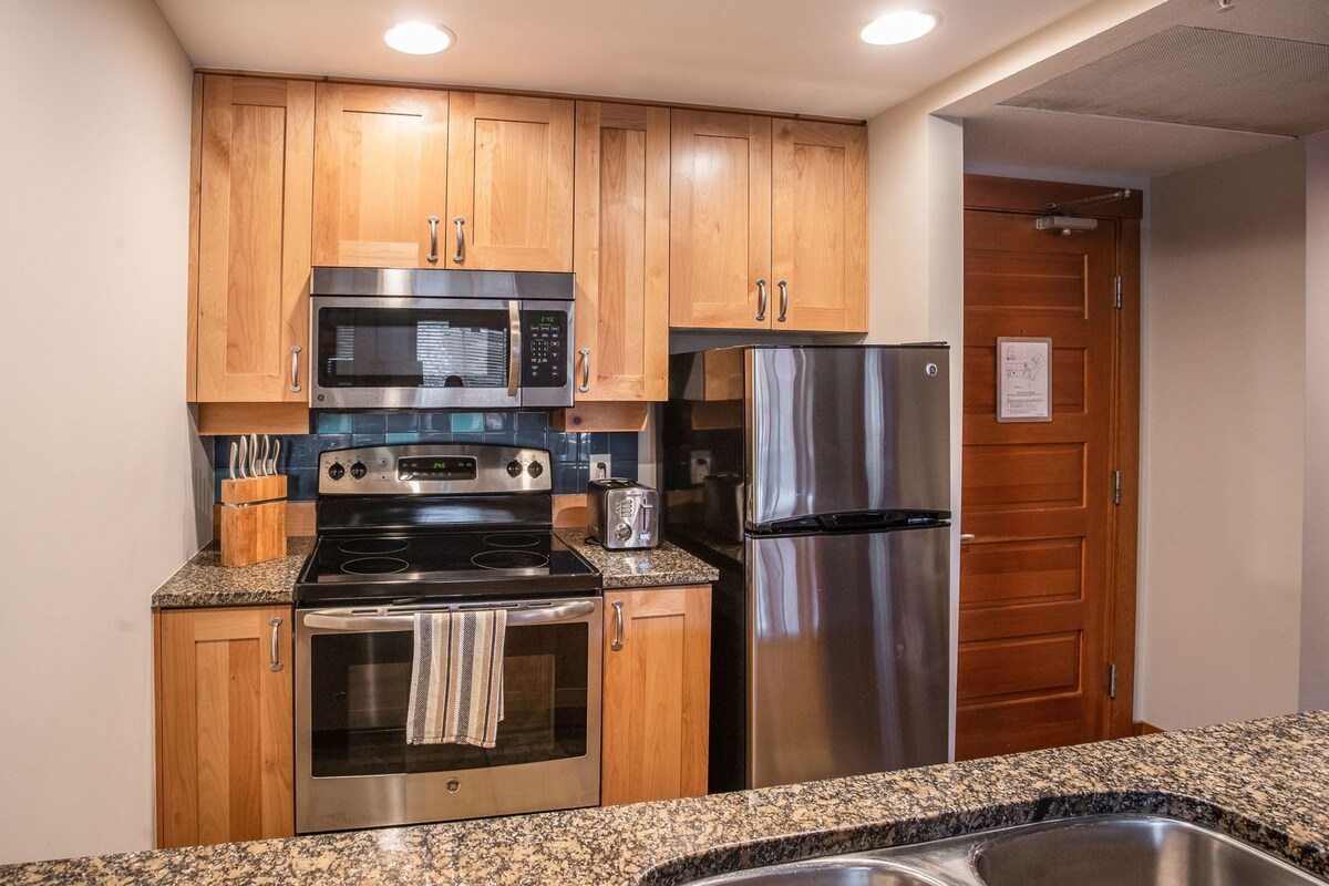 A kitchen with wooden cabinets, stainless steel appliances, granite countertops, and a stainless steel sink.