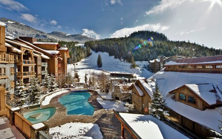 A resort with a pool, wooden buildings, and a snowy mountain backdrop.
