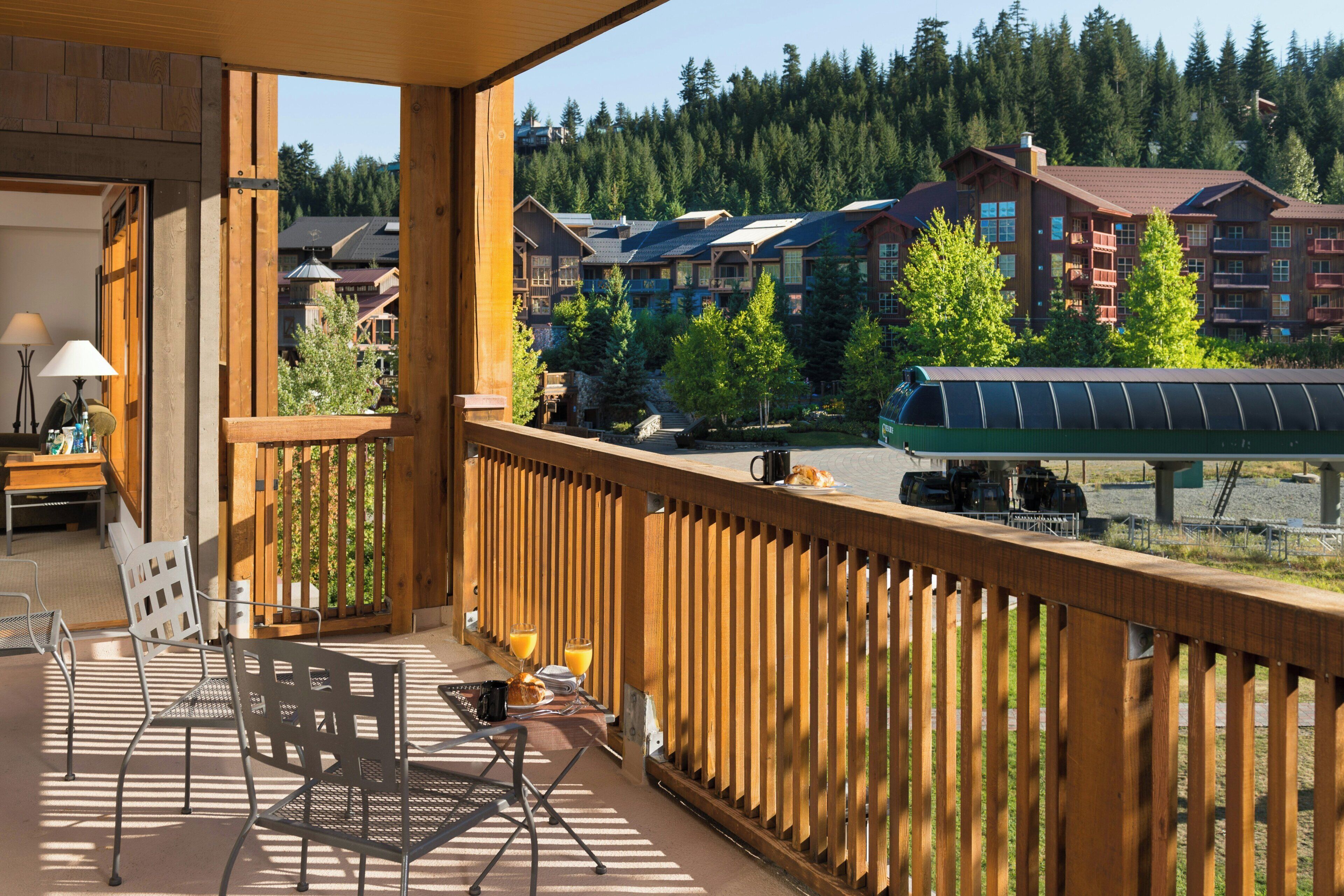 A balcony with outdoor furniture, a view of a forested area, and a building with multiple stories in the background.