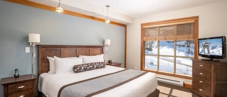 Ein Hotelzimmer mit einem großen Bett, einem hölzernen Kopfteil, zwei Nachttischlampen, einem Fernseher und einem Fenster mit Jalousien.