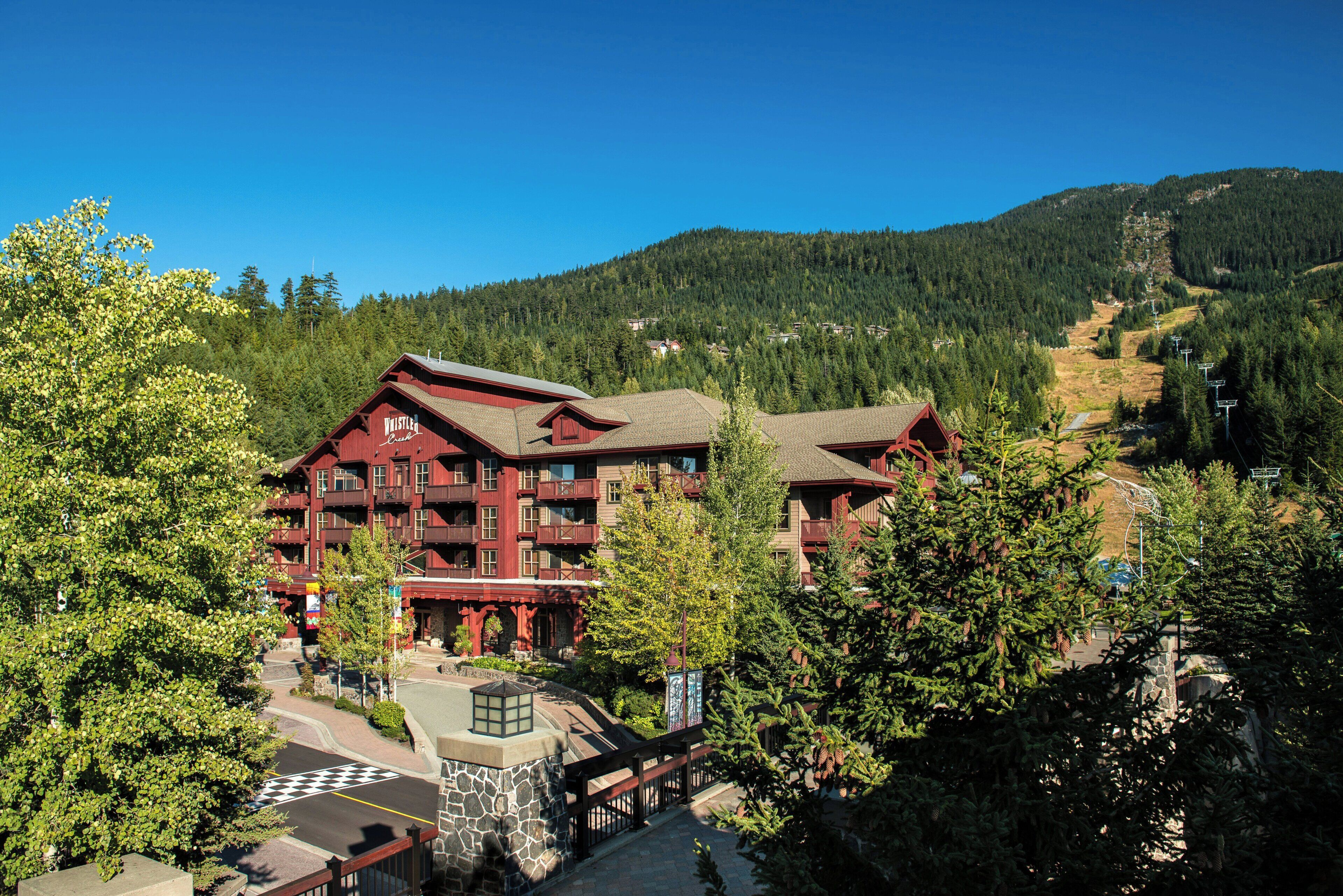 Un chalet à plusieurs étages, doté de balcons, entouré d’arbres et avec une chaîne de montagnes en toile de fond.