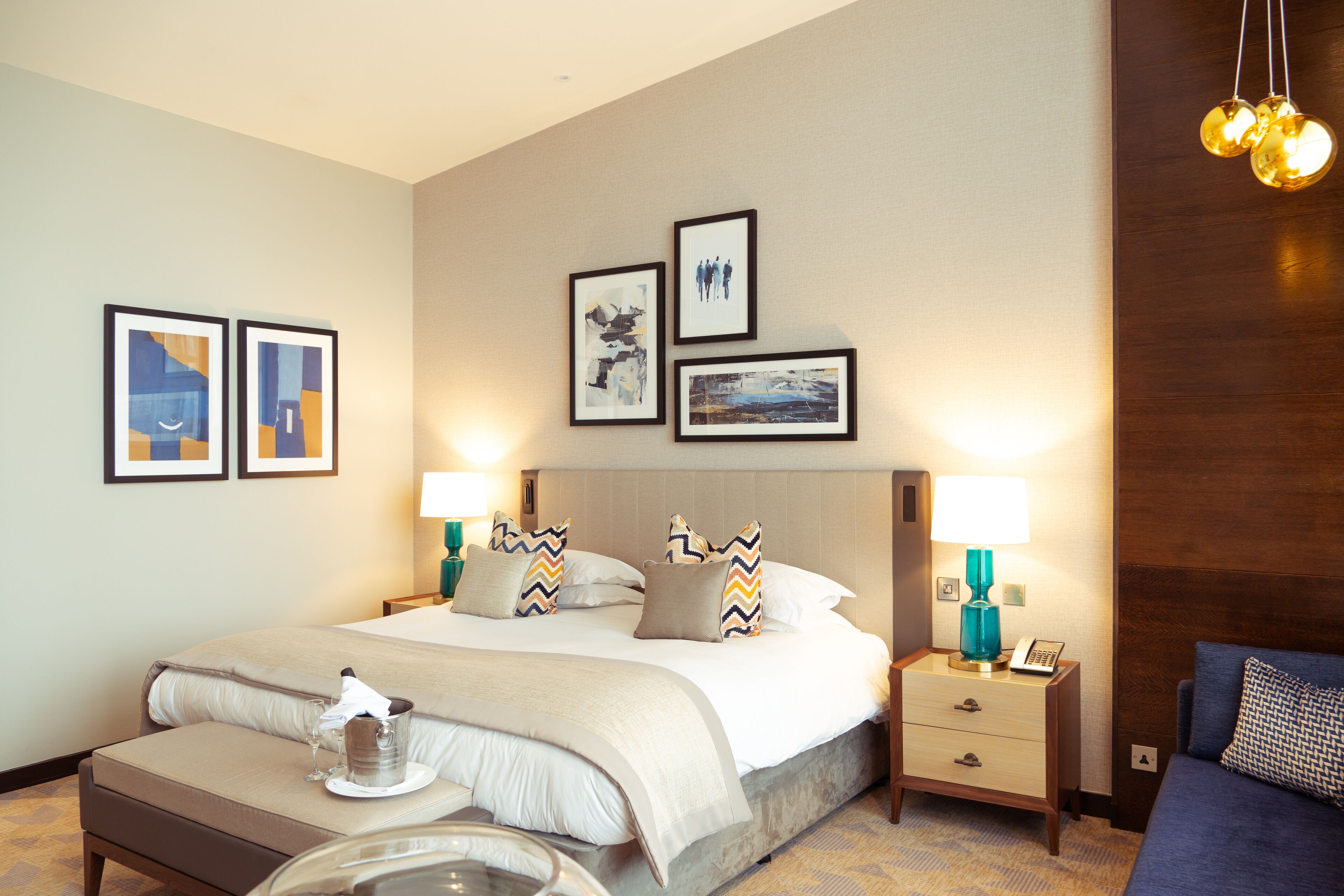 A hotel room with a large bed, bedside tables, a nightstand, and wall art.