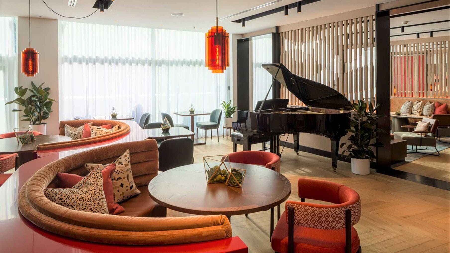 A modern lounge area with a grand piano, comfortable seating, and a large window providing natural light.
