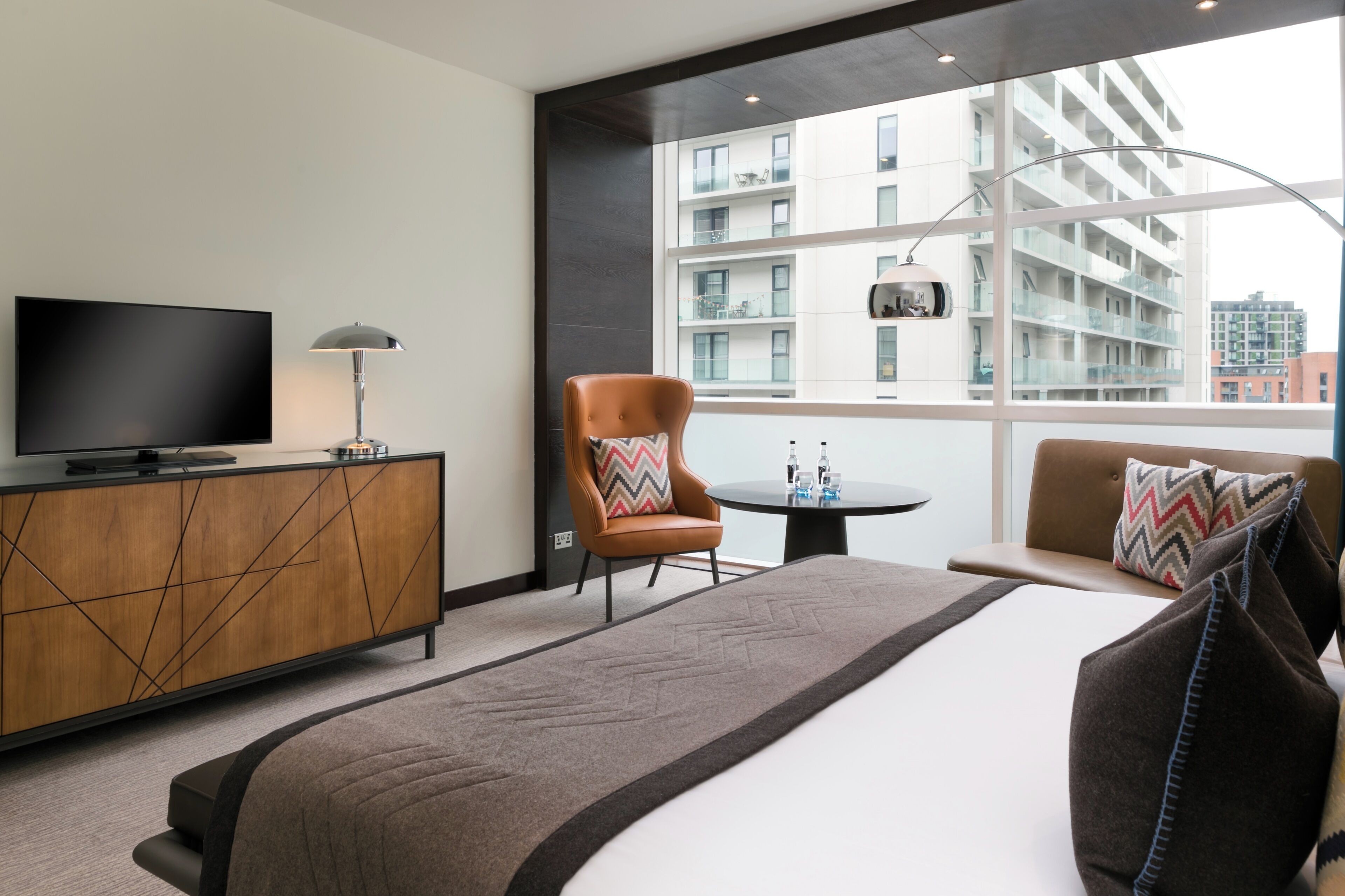 A modern hotel room with a large bed, a TV, a desk, and a chair.