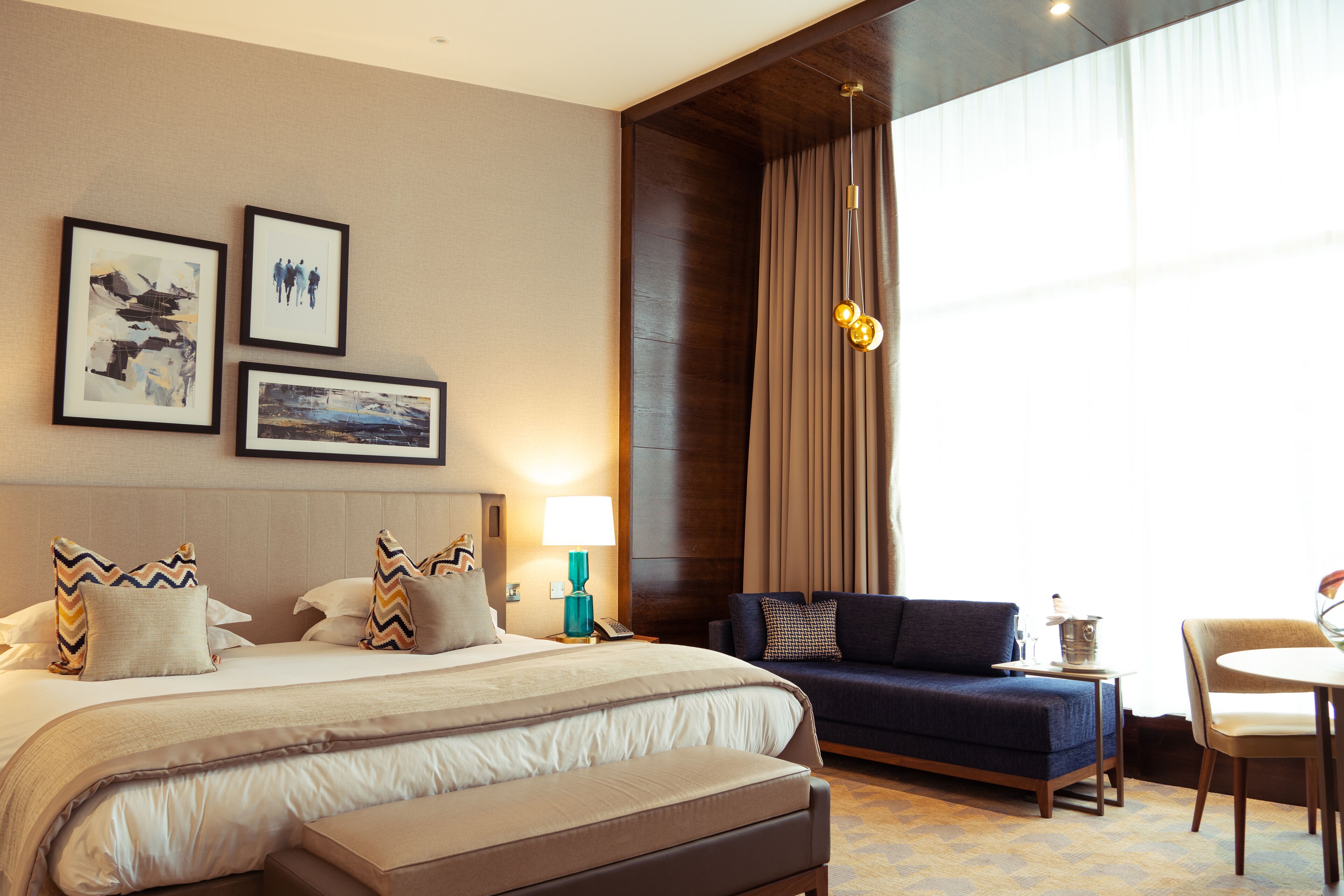 A hotel room with a large bed, a sofa, a dining table, and a chandelier.