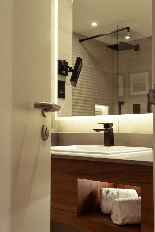 A modern bathroom with a large mirror, a shower, and a wooden vanity.