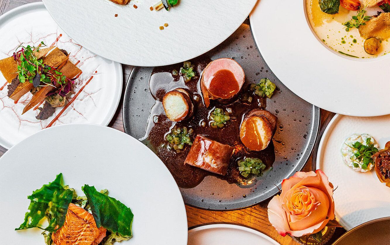 A variety of dishes on plates, including salmon, steak, and other gourmet foods.