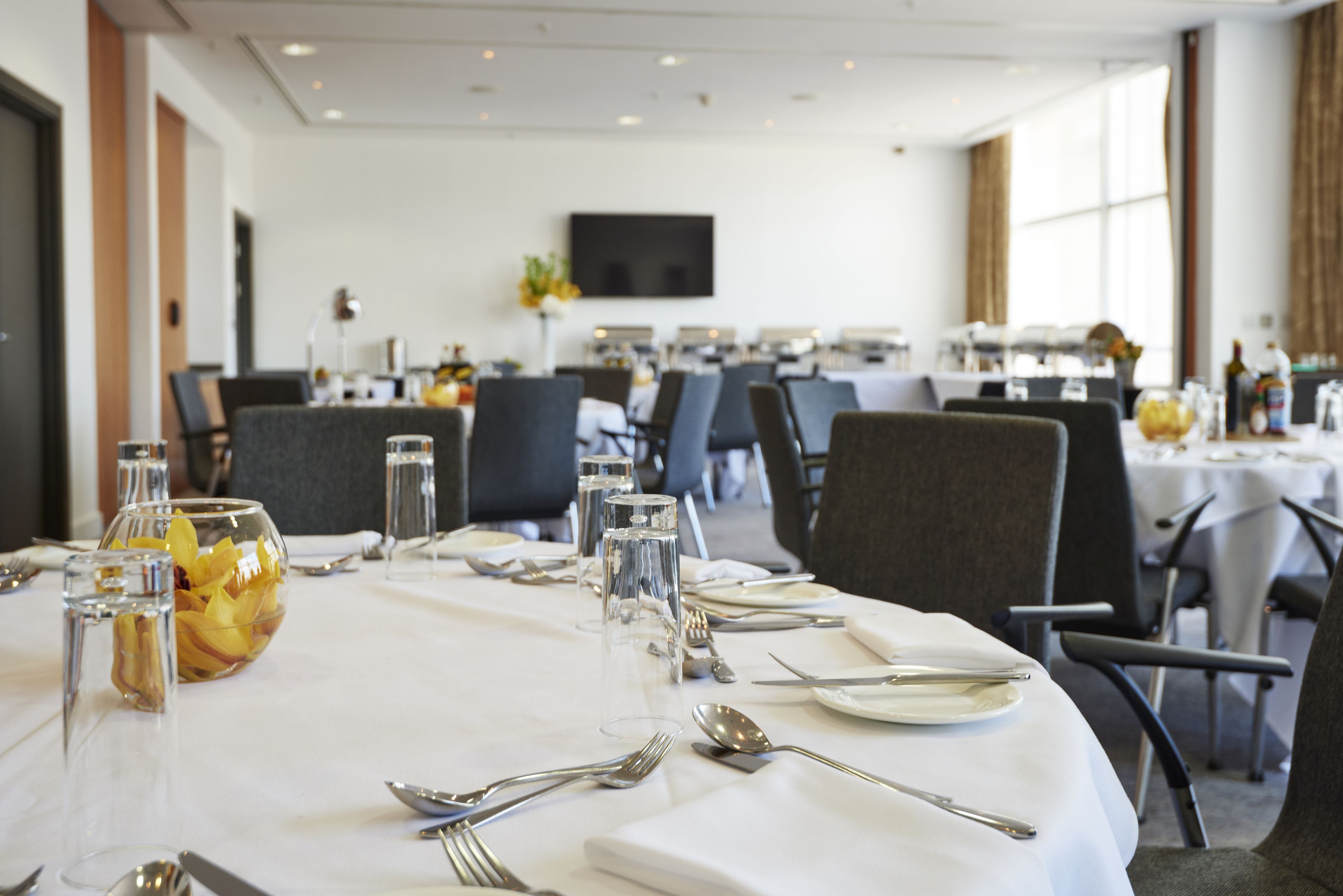 A dining area with round tables set for a meal, including cutlery and glasses.