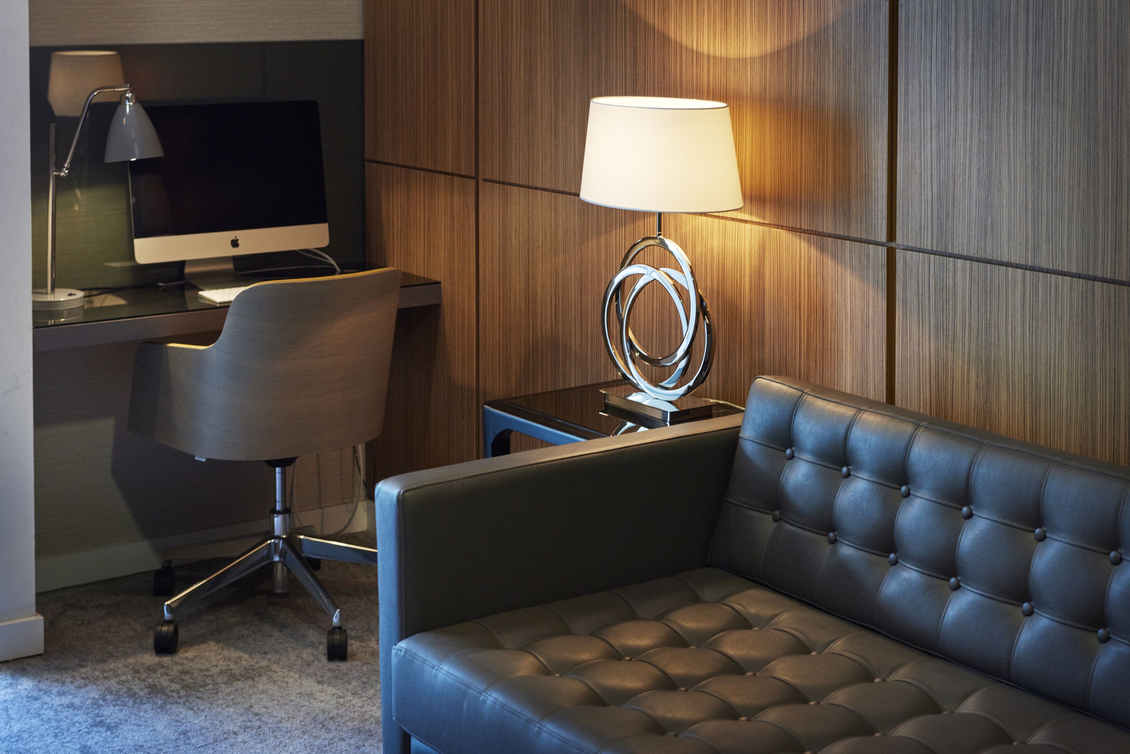 A modern hotel room with a leather sofa, a desk with a computer, and a lamp.
