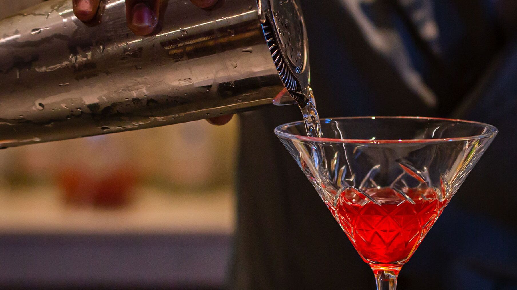 A cocktail being poured into a martini glass.