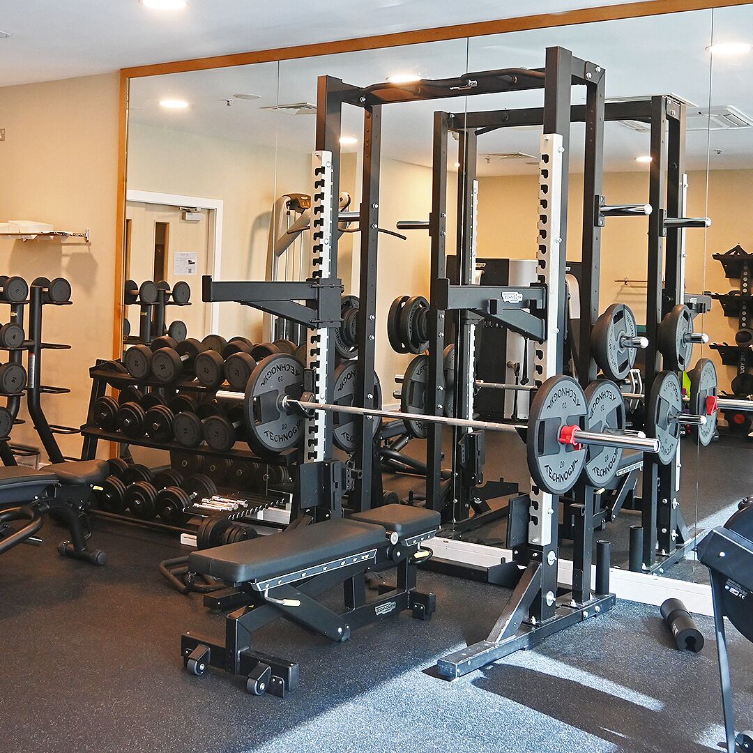 A gym with weightlifting equipment, including a squat rack and dumbbells.