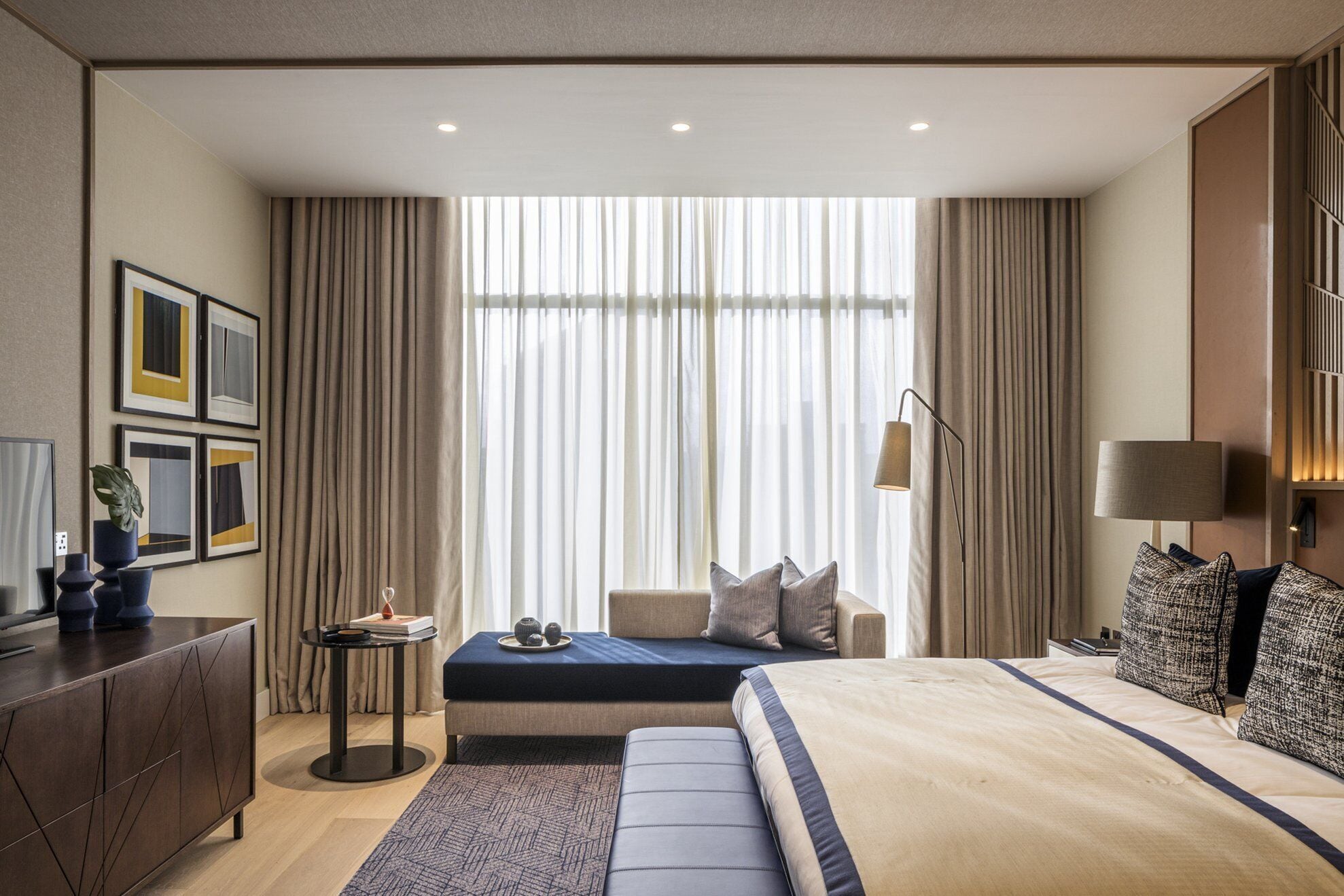 A modern hotel room with a large bed, a sofa, a desk, and a large window with curtains.