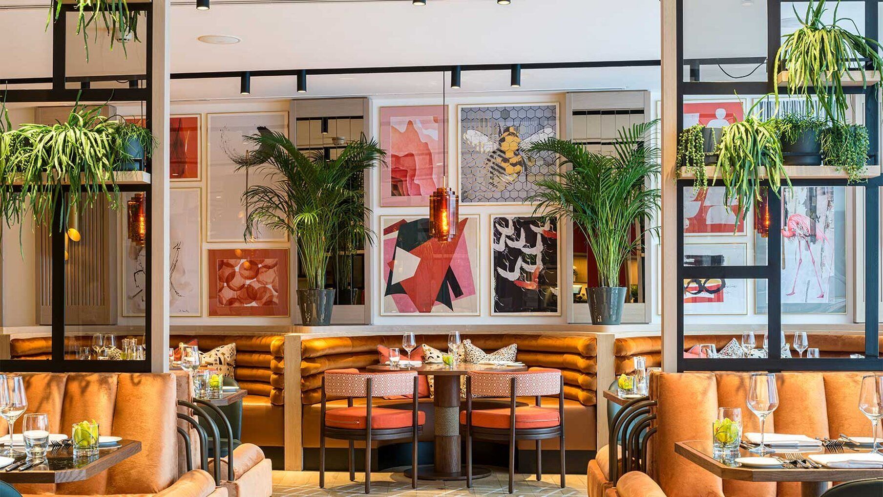 A restaurant with booths and tables, framed artwork on the walls, and potted plants.