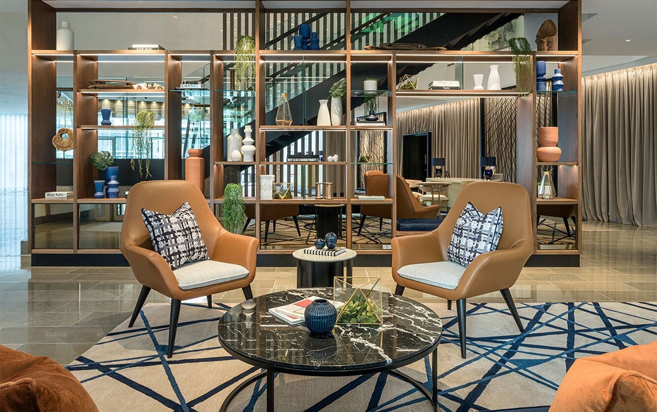 Um lobby moderno com dois poltronas de couro, uma mesa de centro de mármore e um tapete estampado.