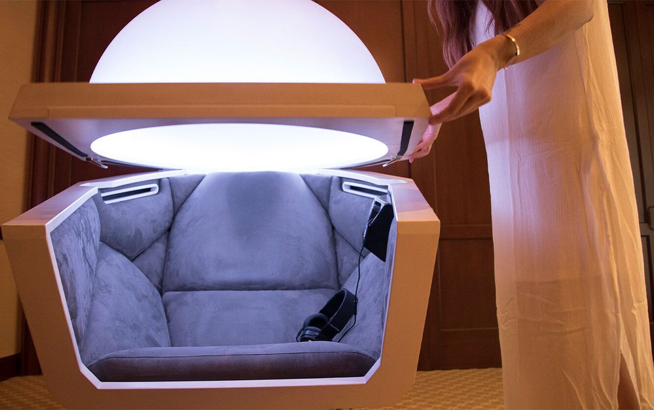 A futuristic chair with a large overhead light, a remote control, and a power outlet.