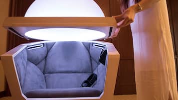 A futuristic chair with a large overhead light, a remote control, and a power outlet.