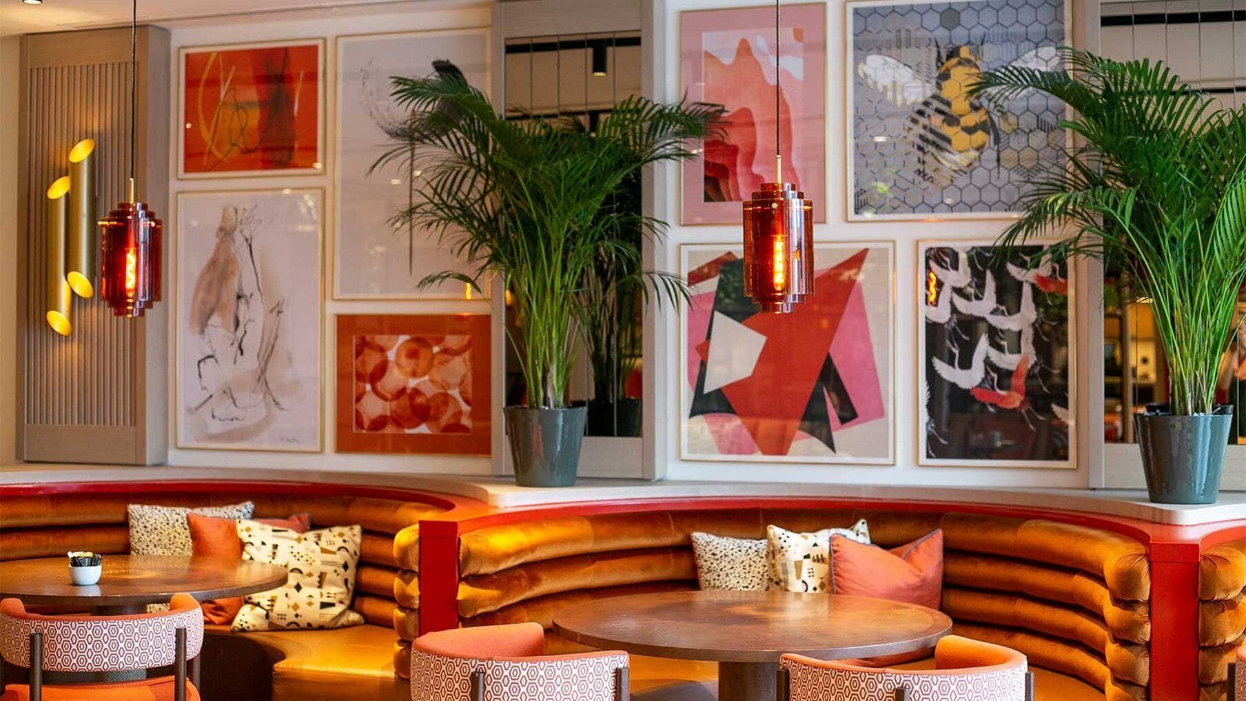 A modern interior with a curved seating area, framed artwork on the walls, and potted plants.