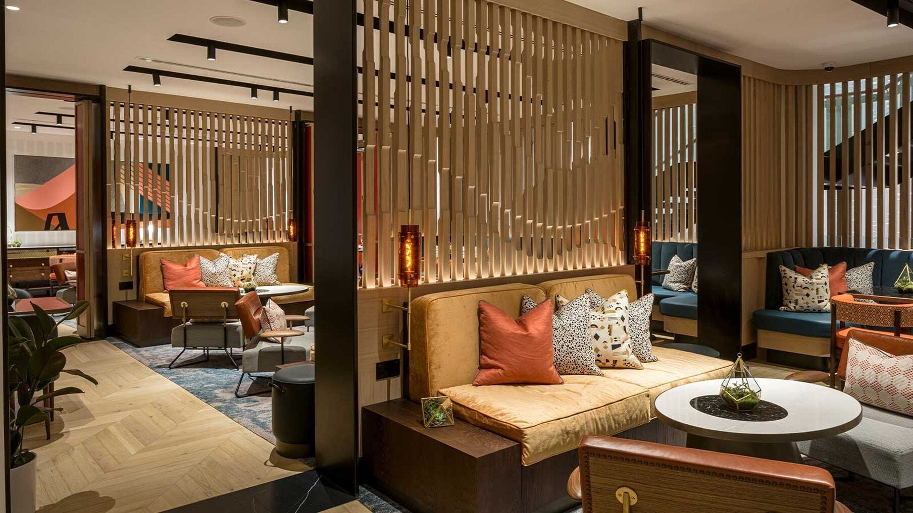 A modern hotel lobby with a central seating area featuring sofas and armchairs, a wooden partition wall, and a staircase in the background.