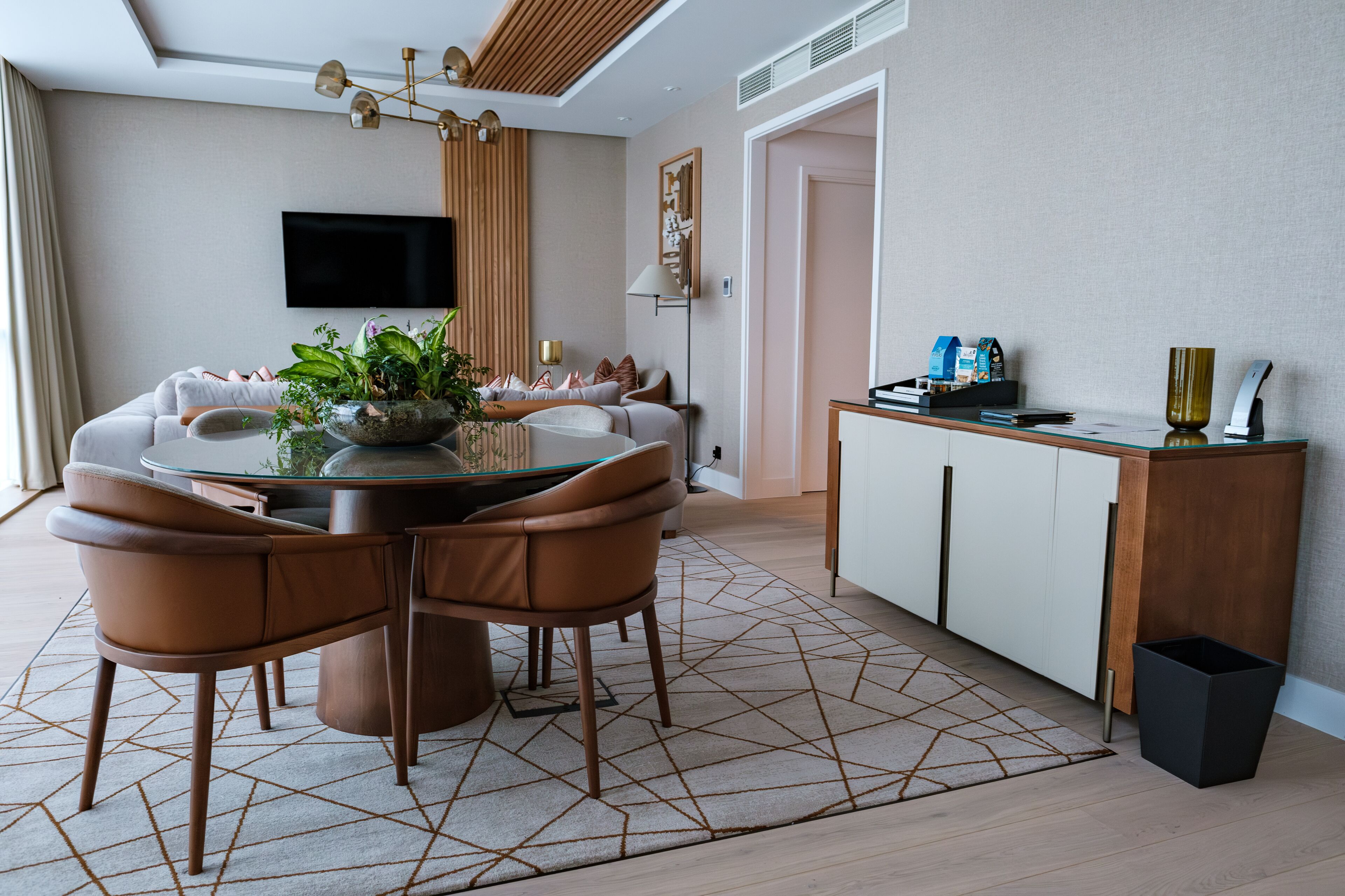 A modern living room with a round dining table, brown leather chairs, a glass coffee table, and a large potted plant.