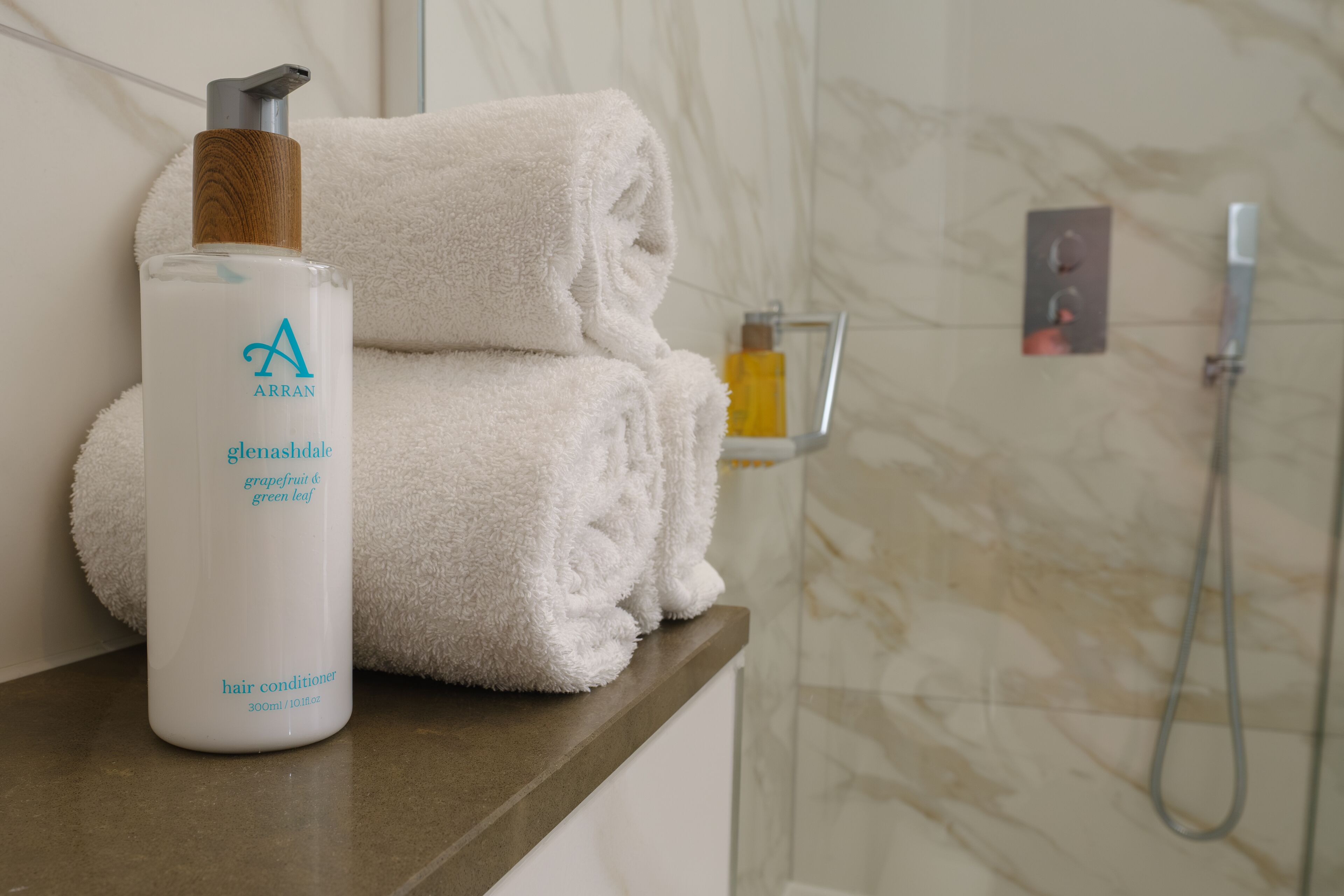 A bathroom with a white towel, a bottle of hair conditioner, and a shower head.