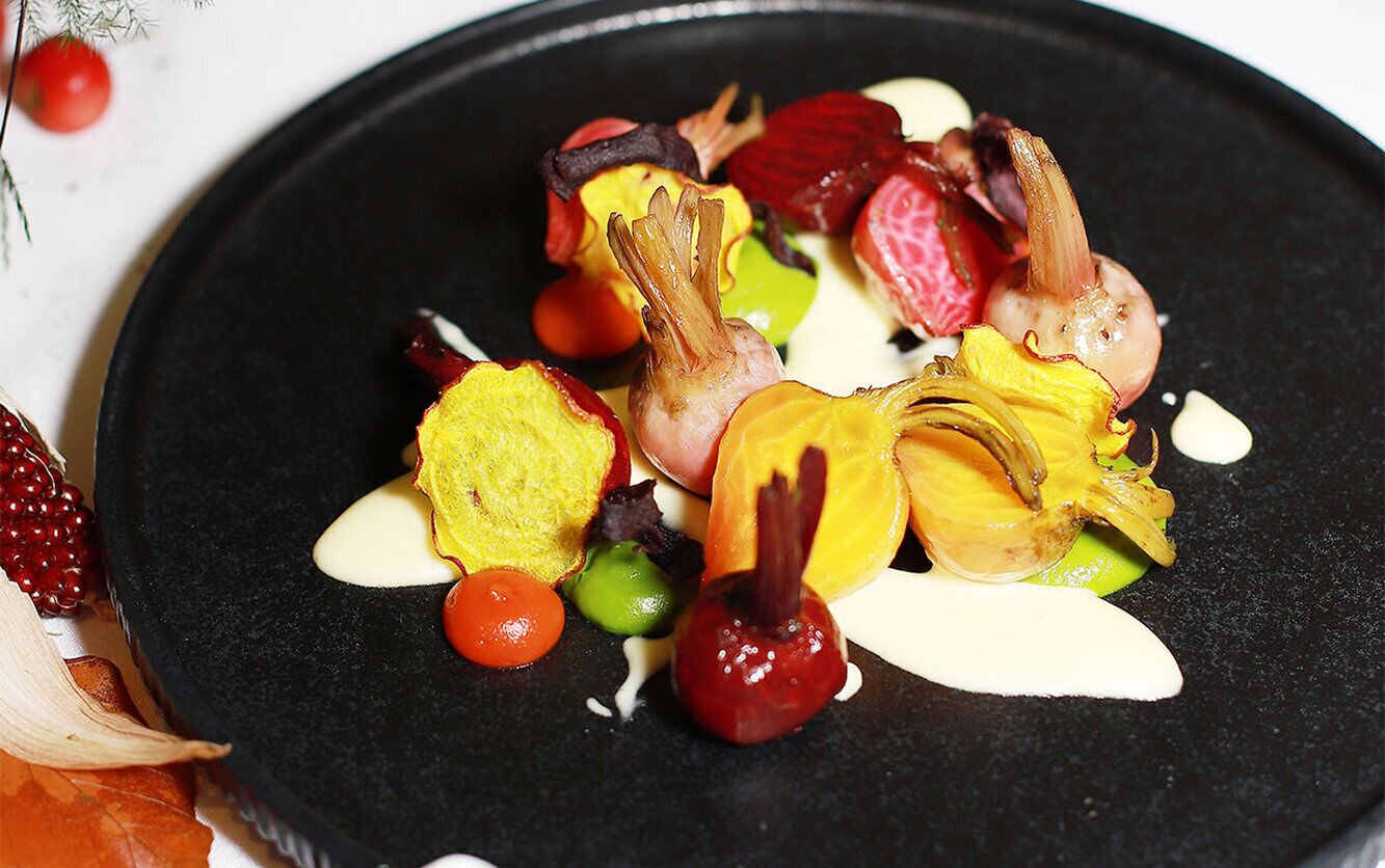 A black plate with various food items including vegetables and a creamy sauce.
