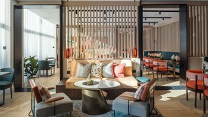 A modern lounge area with a sofa, two armchairs, a coffee table, and a dining area with red chairs and a table. - The Lowry Hotel Manchester (Manchester)