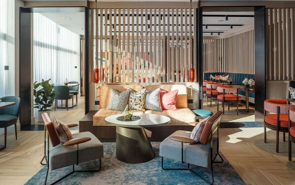 A modern lounge area with a sofa, two armchairs, a coffee table, and a dining area with red chairs and a table. - The Lowry Hotel Manchester (Manchester)