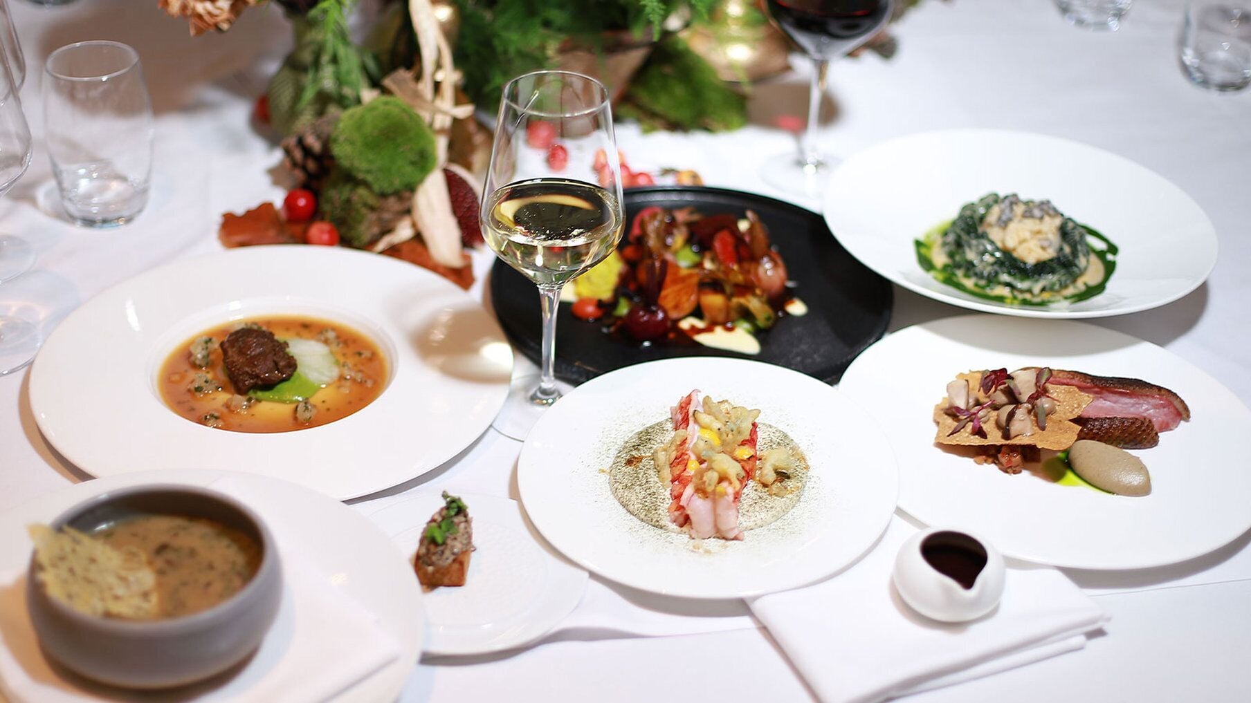 Una mesa servida con diversos platos, una copa de vino blanco y una vela.
