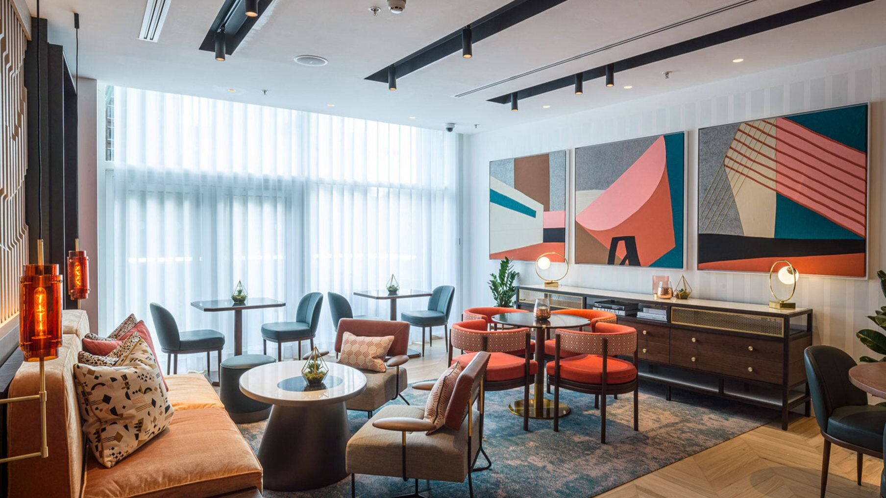 A modern hotel lobby with a large window, a sofa, multiple chairs, a coffee table, and a desk with a lamp.