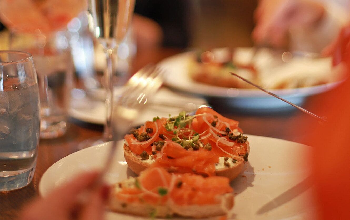 A close-up of a plate with a food item, possibly a sandwich or appetizer, garnished with green herbs and thinly sliced onions.