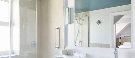 A modern bathroom with a glass-enclosed shower, a large mirror, and a white vanity with a marble countertop.