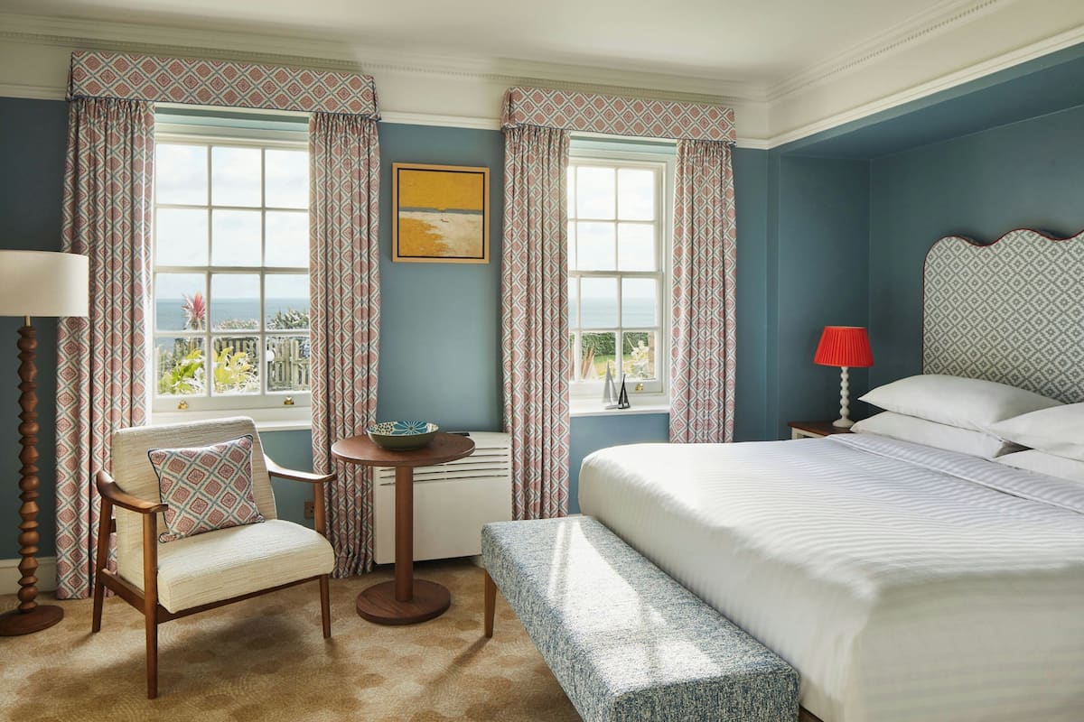 A bedroom with a bed, a chair, a table, and curtains.