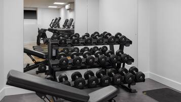 A gym with a bench press, a rack of dumbbells, and a treadmill.