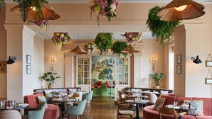A restaurant with round tables, cushioned seating, hanging plants, and a mural on the wall.
