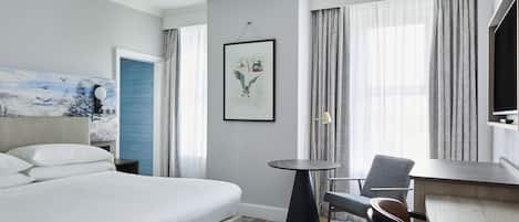 Una habitación de hotel con una cama grande, una mesita redonda pequeña, una silla, un escritorio y un televisor.