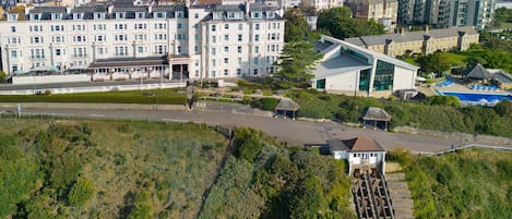 A coastal hotel with a large building, a swimming pool, and a train station.