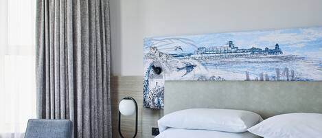 A hotel room with a bed, a chair, a nightstand with a lamp, and a painting on the wall.