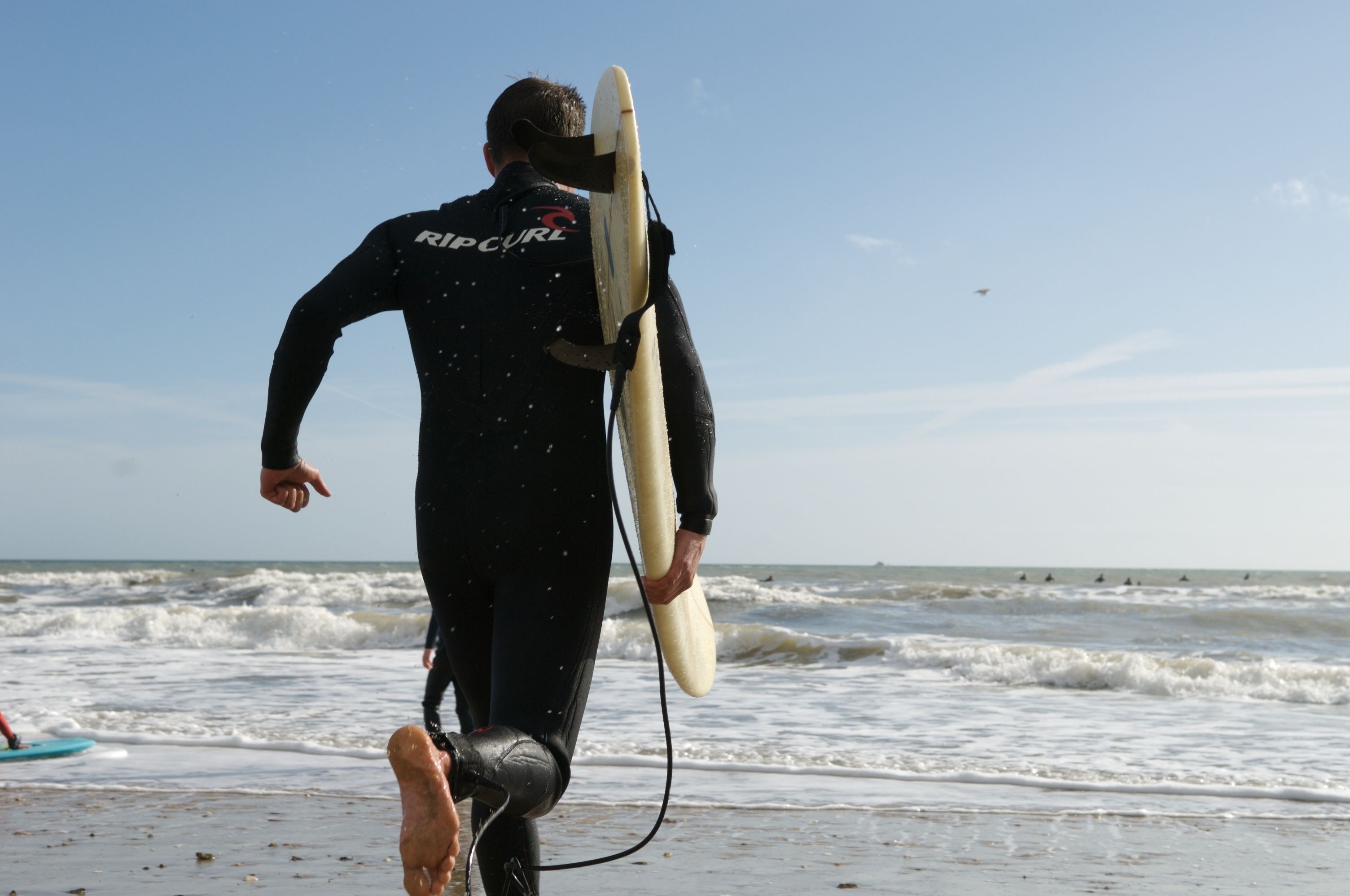 Une personne portant une combinaison de plongée et transportant une planche de surf sur une plage.