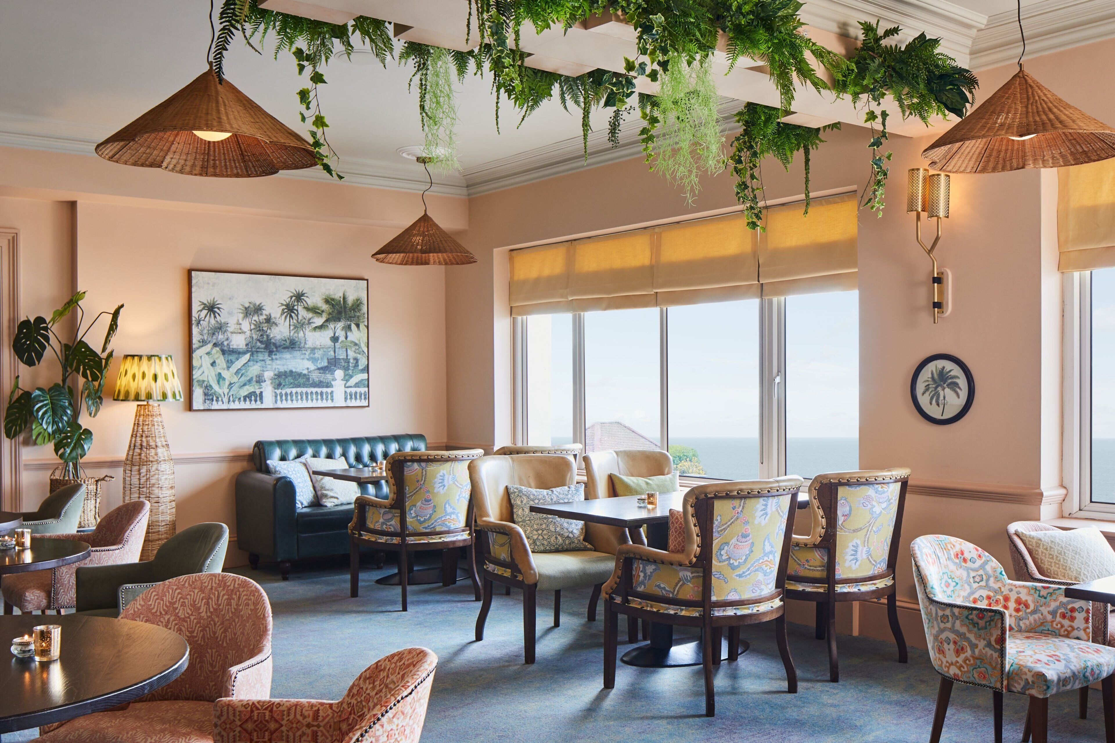 A room with a large window, a sofa, multiple chairs, a table, and hanging plants.