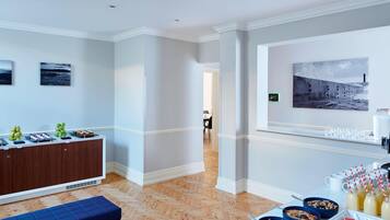 Una habitación de hotel moderna con piso de madera en diseño de espiga, un banco acolchado azul, una mesa de buffet con comida y bebidas, y un cuadro abstracto grande en la pared.