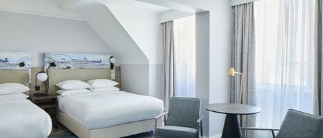 Habitación de hotel con dos camas, una mesa redonda, dos sillas, una lámpara y un cuadro en la pared.