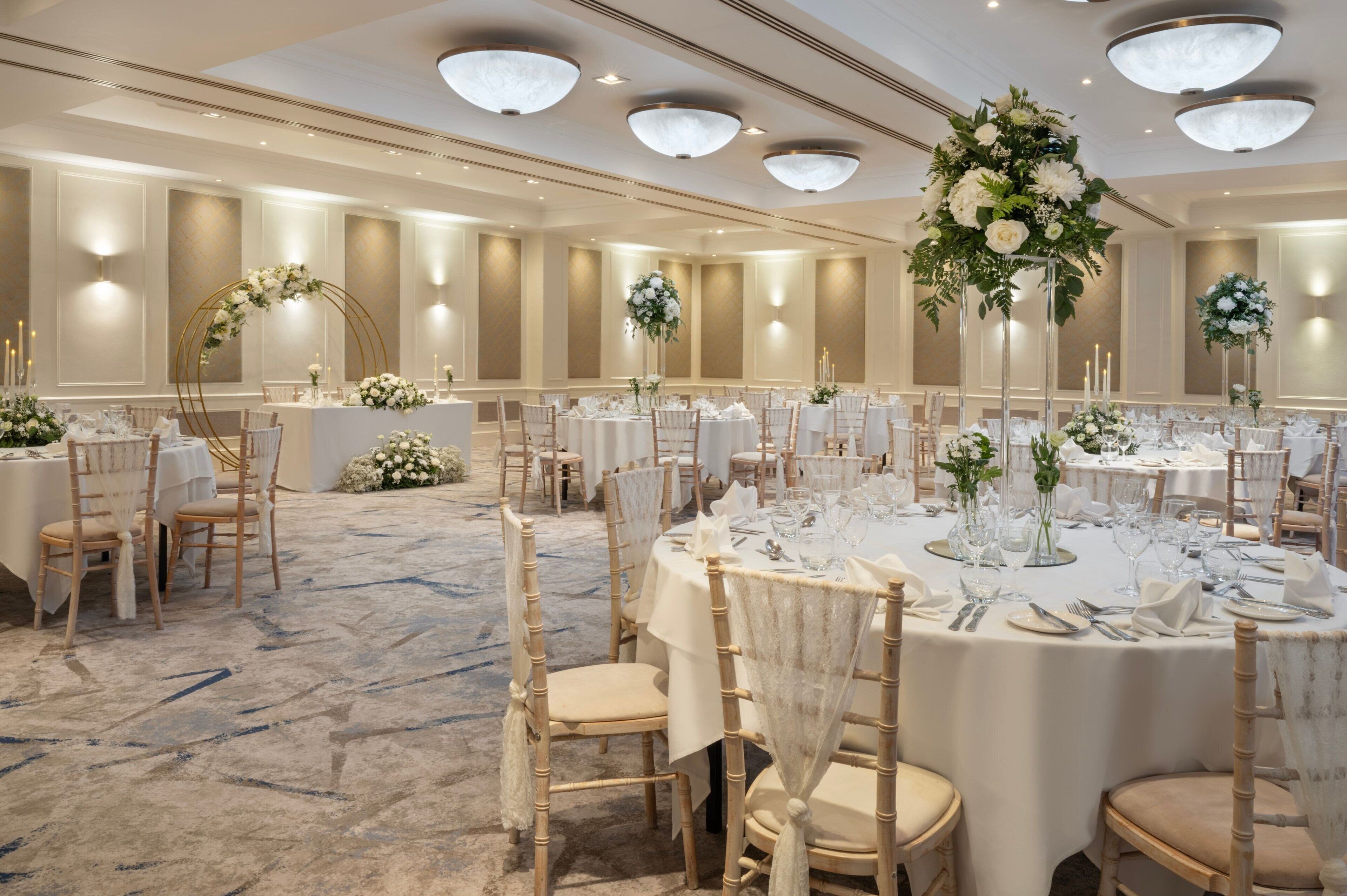 A banquet hall with round tables, white tablecloths, and floral centerpieces.