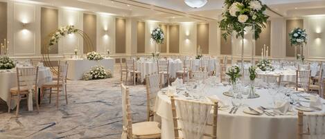 A banquet hall with round tables, white tablecloths, and floral centerpieces.
