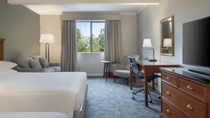 Hotelkamer met twee bedden, een bureau, een stoel, een televisie en een raam met gordijnen.
