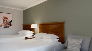 Una habitación de hotel con dos camas, un cabecero de madera, un sillón gris y un cuadro enmarcado en la pared.