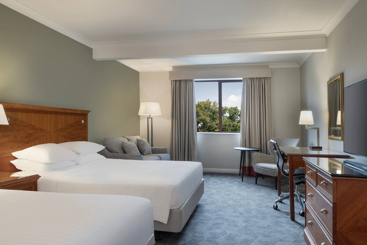 Une chambre d’hôtel avec deux lits, un bureau, une chaise, une commode et une fenêtre avec des rideaux.