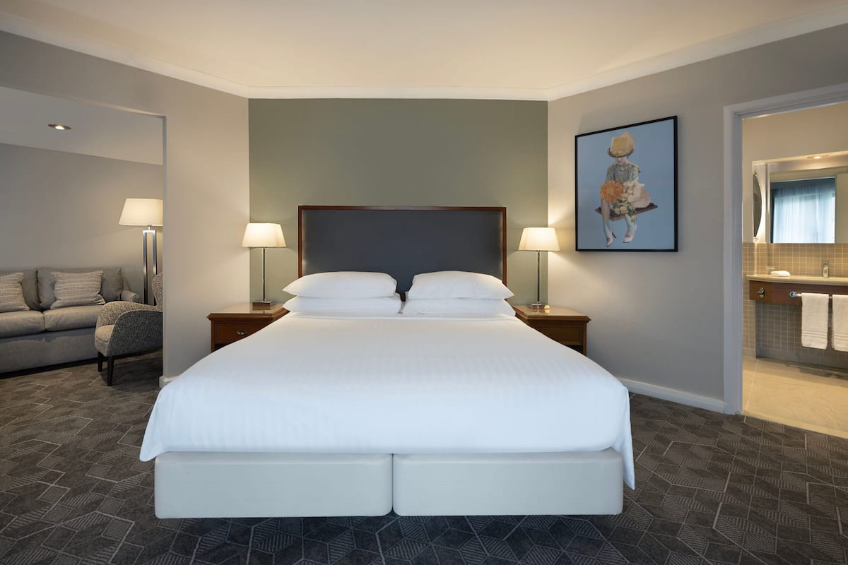 Une chambre d’hôtel avec un grand lit, deux tables de chevet avec des lampes, un canapé et une salle de bain équipée d’un miroir et d’un porte-serviettes.