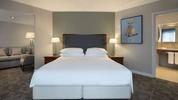 Habitación de hotel con una cama grande, dos mesitas de noche con lámparas, un sofá y un baño con espejo y toallero.